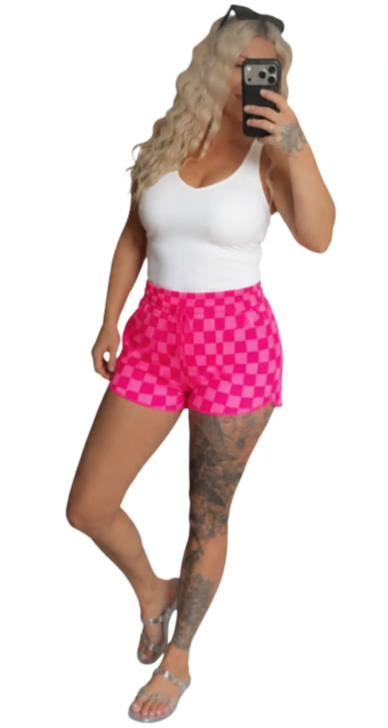 Hot pink checkerboard drawstring shorts worn with a white tank top and silver sandals.